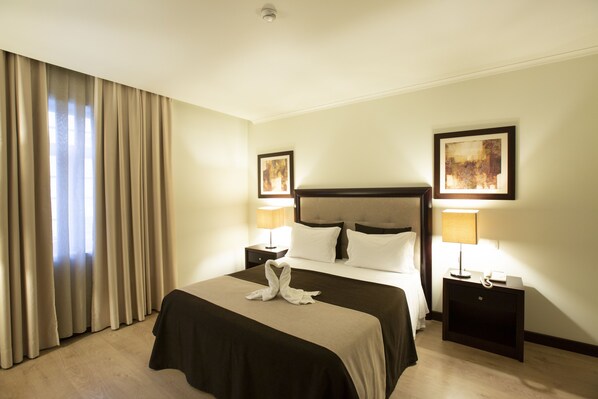 A hotel room with a large bed, two bedside tables with lamps, a headboard, and two framed pictures on the walls. - Veneza Hotel (Aveiro)