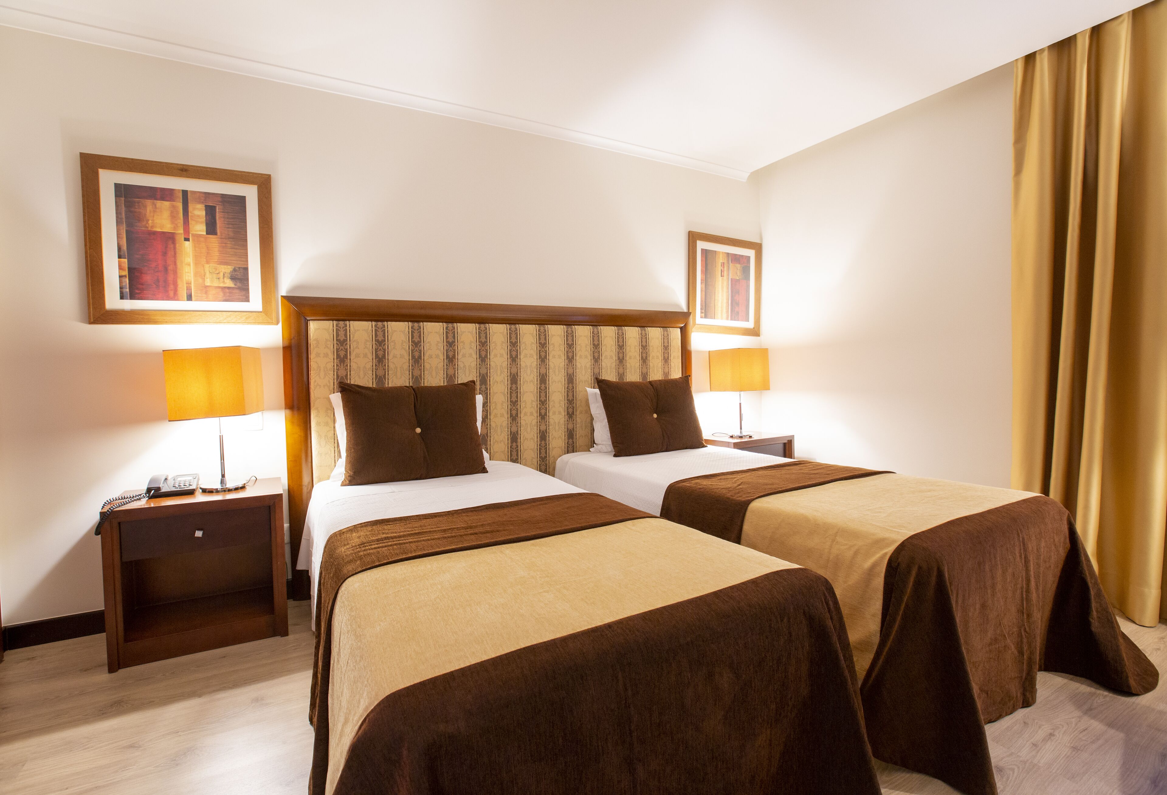 Habitación de hotel con dos camas, cabecero de madera, lámparas de noche, mesita de noche con teléfono y un cuadro en la pared.
