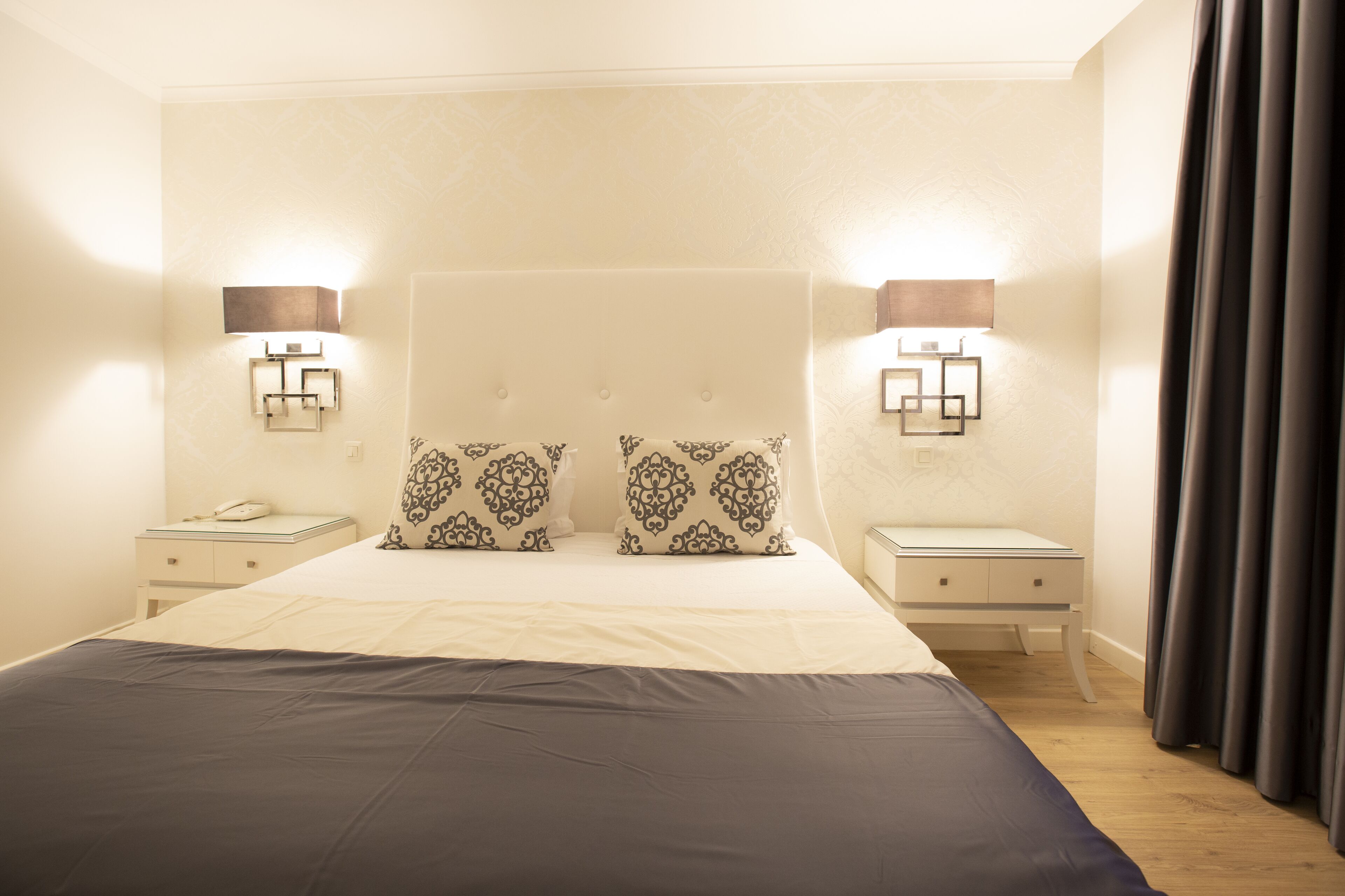 A hotel room with a large bed, two bedside tables, a nightstand, and two wall-mounted lamps.
