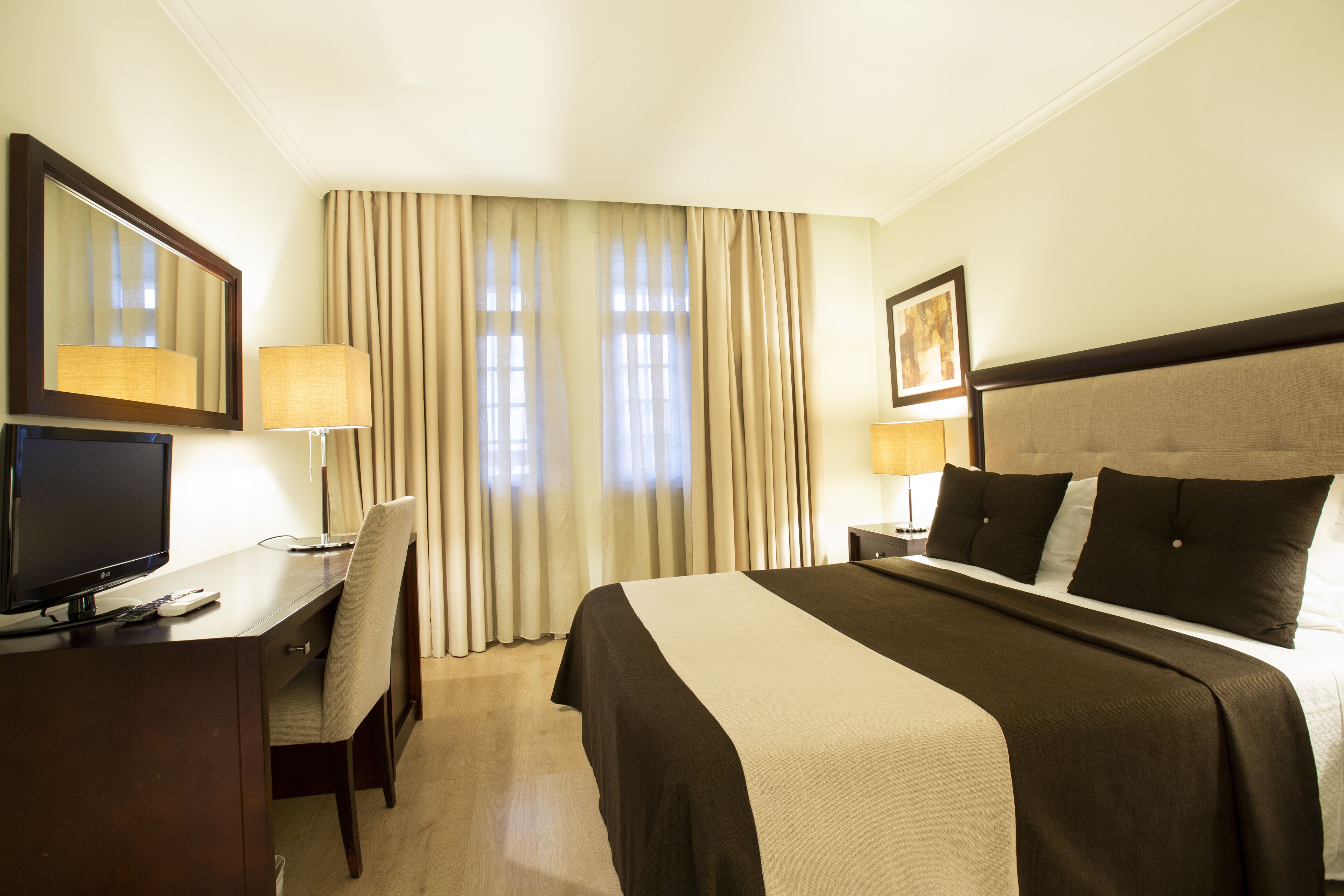 A hotel room with a bed, a desk with a computer, a chair, and a television.