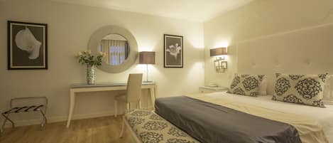 A hotel room with a bed, a desk with a chair, a mirror, and framed artwork on the walls.