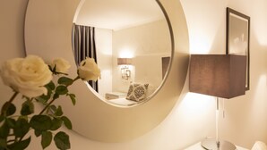 Un miroir rond reflétant une pièce, une lampe de chevet et une rose blanche.