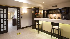 Un espace bar moderne avec deux tabourets, un comptoir où sont exposées différentes bouteilles et un vase décoratif avec des fleurs.