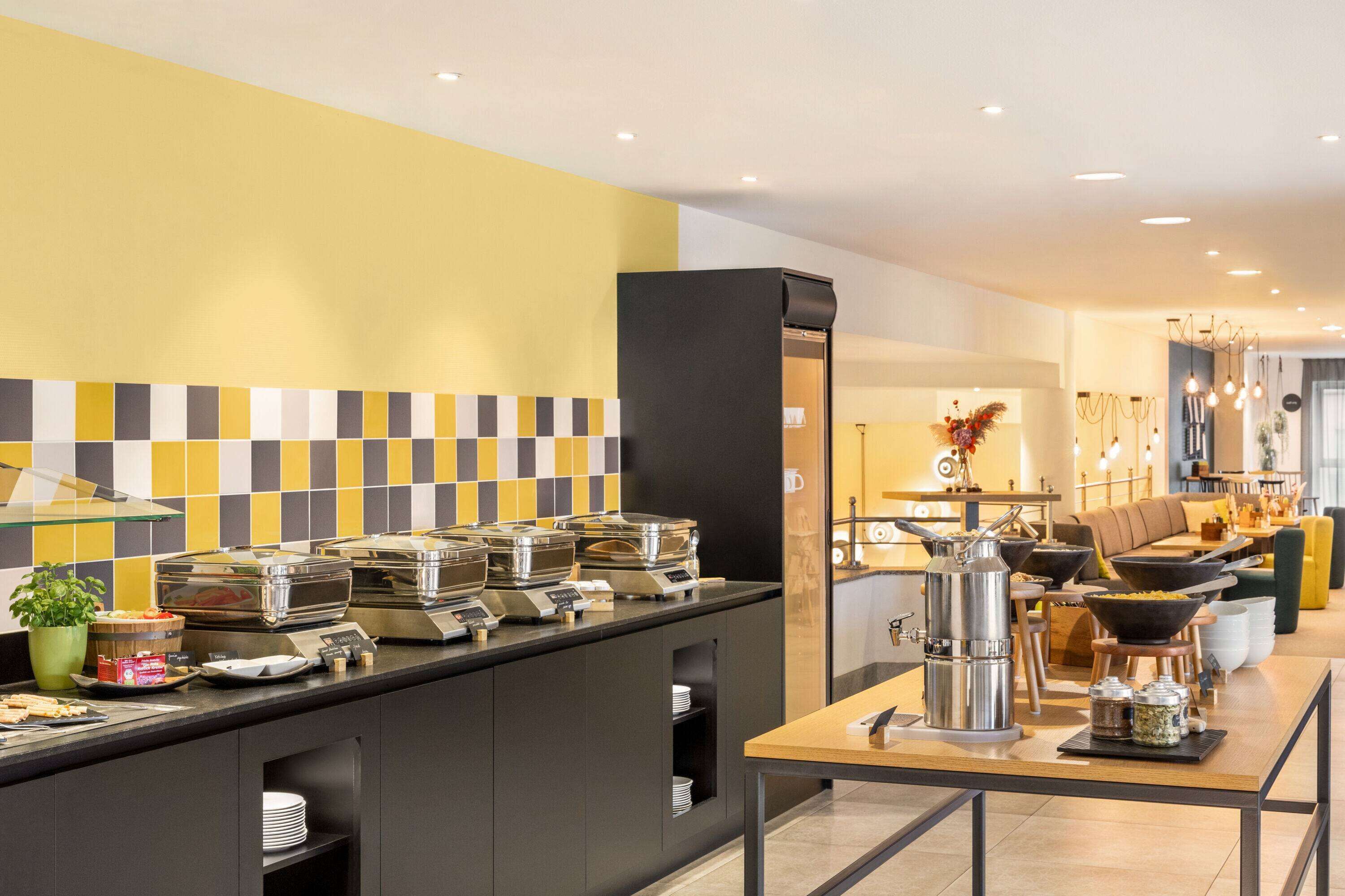A modern hotel room with a breakfast bar, a sofa, and a dining area.