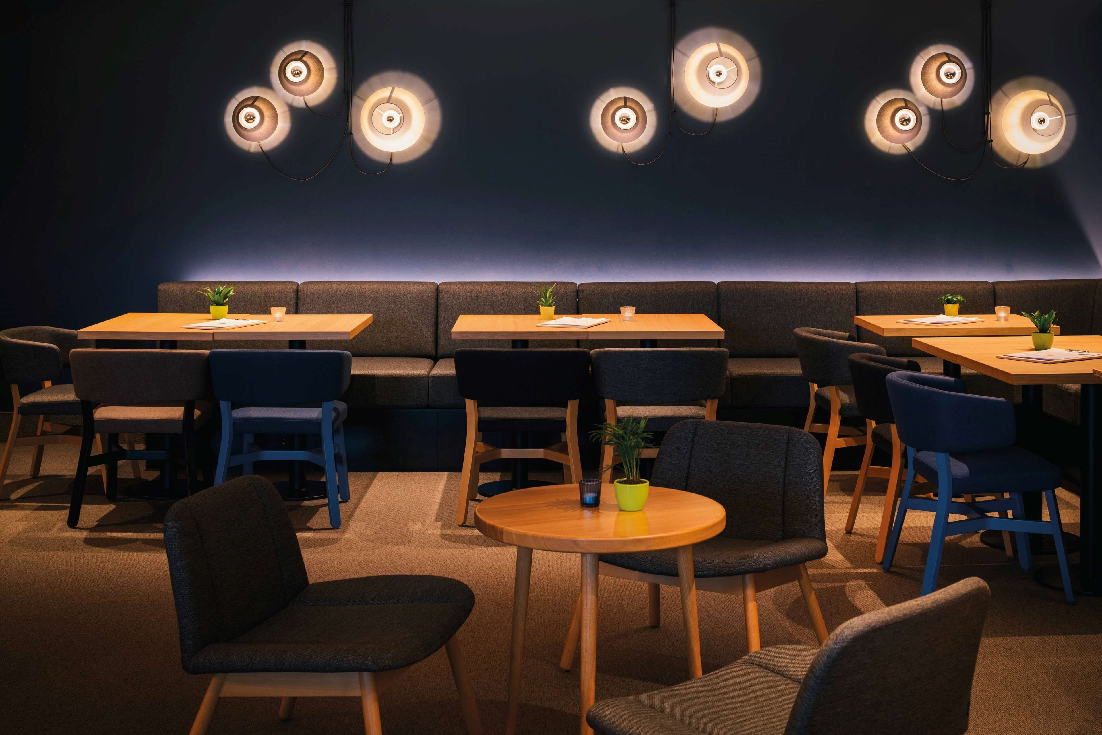 A modern restaurant with booths and tables, ambient lighting, and potted plants.