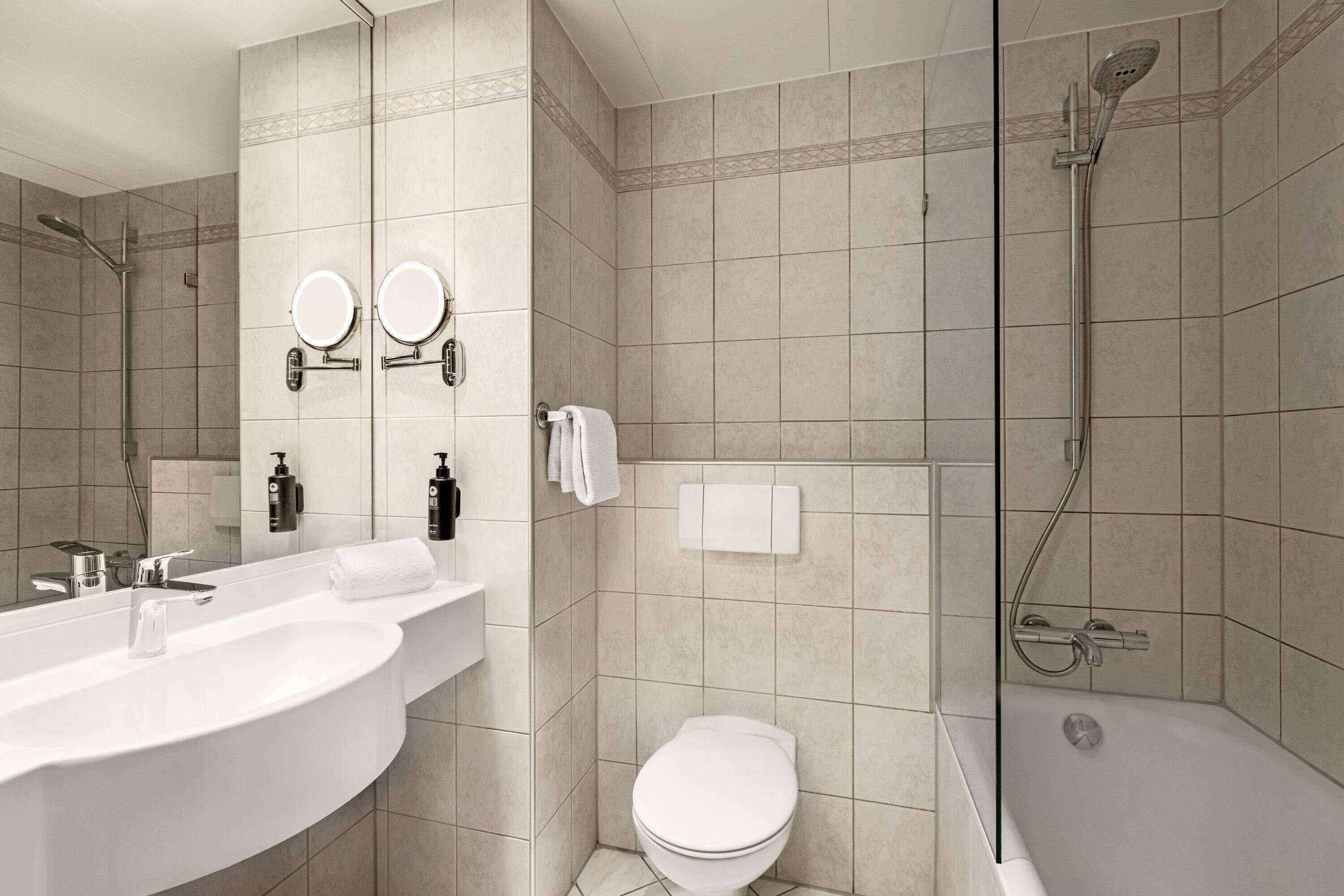 Un baño moderno con un lavamanos grande, dos espejos, un inodoro y una ducha.