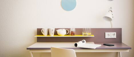 Una habitación moderna con escritorio, silla y estante con tazas y una lámpara.