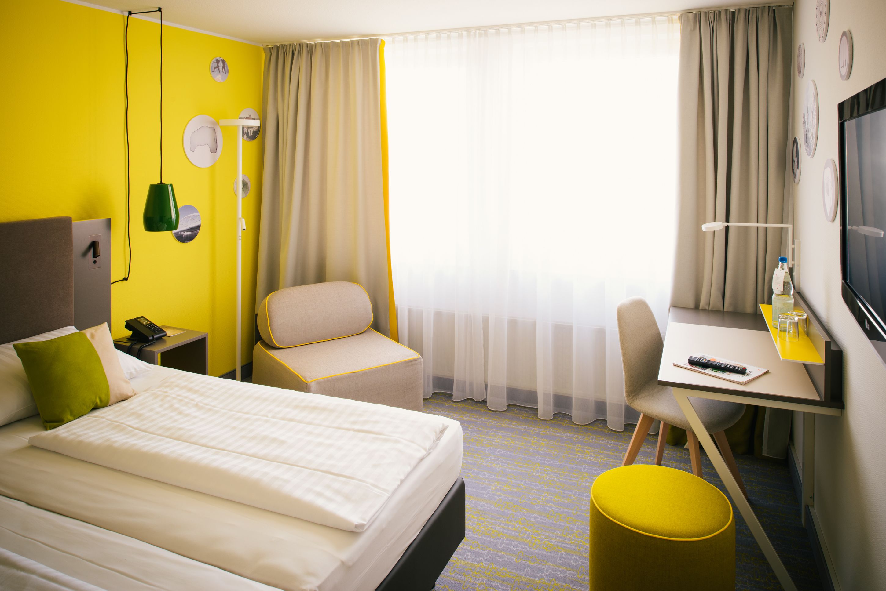 Une chambre d’hôtel comprenant un lit, un bureau, une chaise, une petite table, un téléviseur et une fenêtre avec des rideaux.