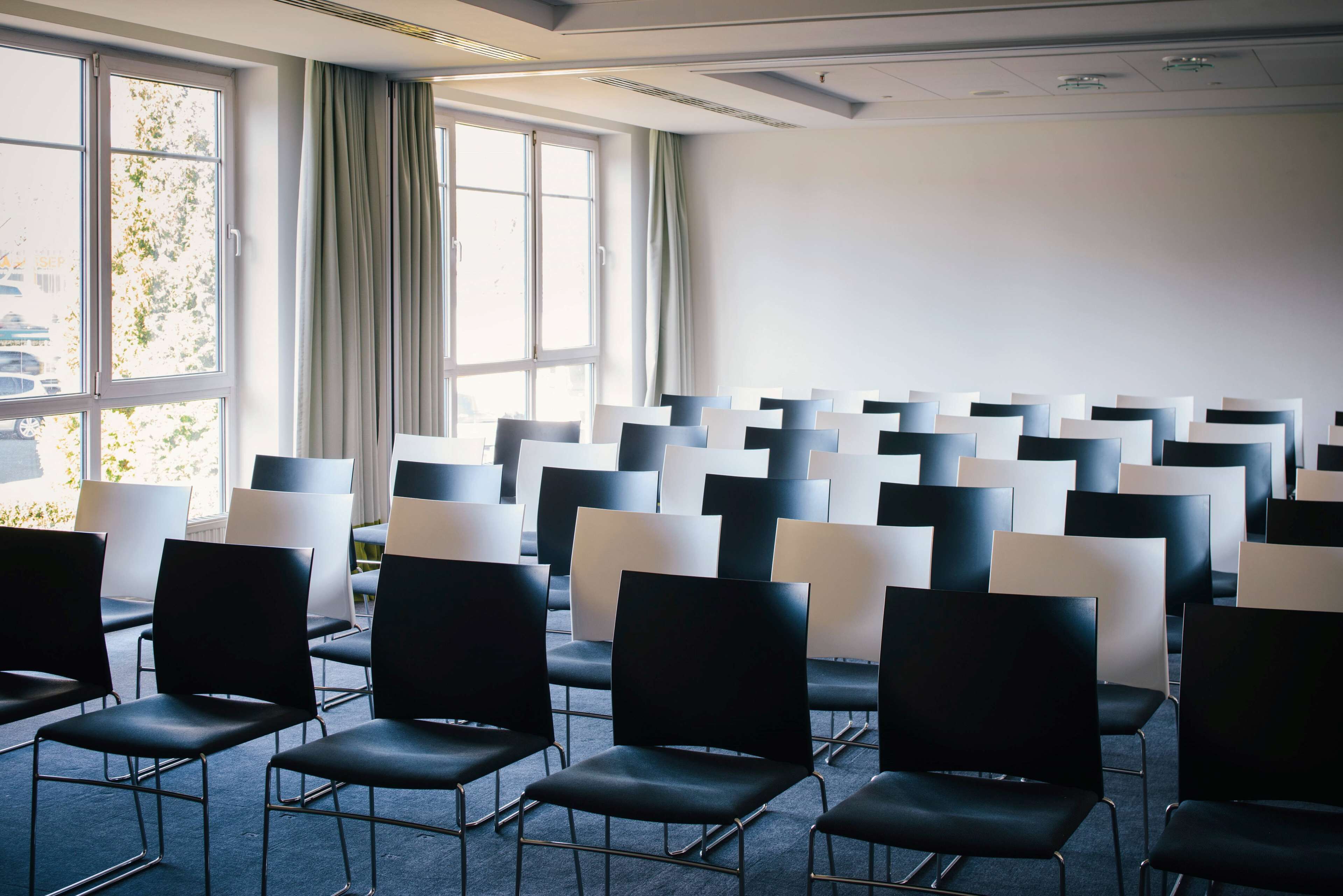 A conference room with rows of chairs, large windows, and a plain wall.