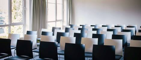 A conference room with rows of chairs, large windows, and a plain wall.