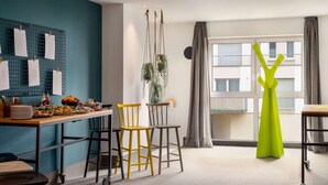 Una habitación moderna con una pared de acento color aguamarina, un comedor con una mesa y sillas de madera, una planta colgante y un ventanal con cortinas.