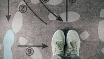 A person standing on a patterned carpet with directional arrows and numbered circles.