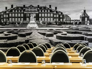 A formal garden with a maze, a large building with classical architecture, and rows of tables with chairs.