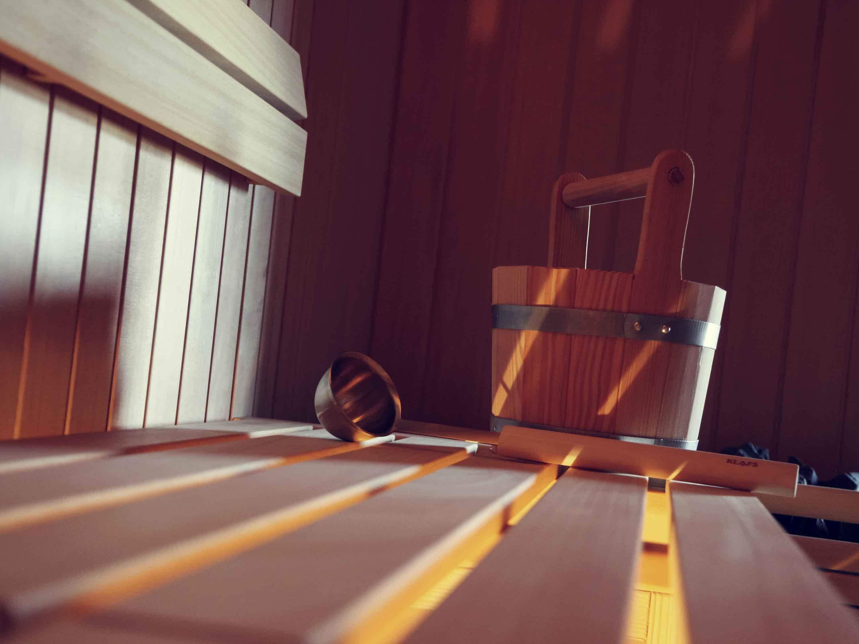 A wooden sauna with a metal bucket and a metal bowl on a bench.