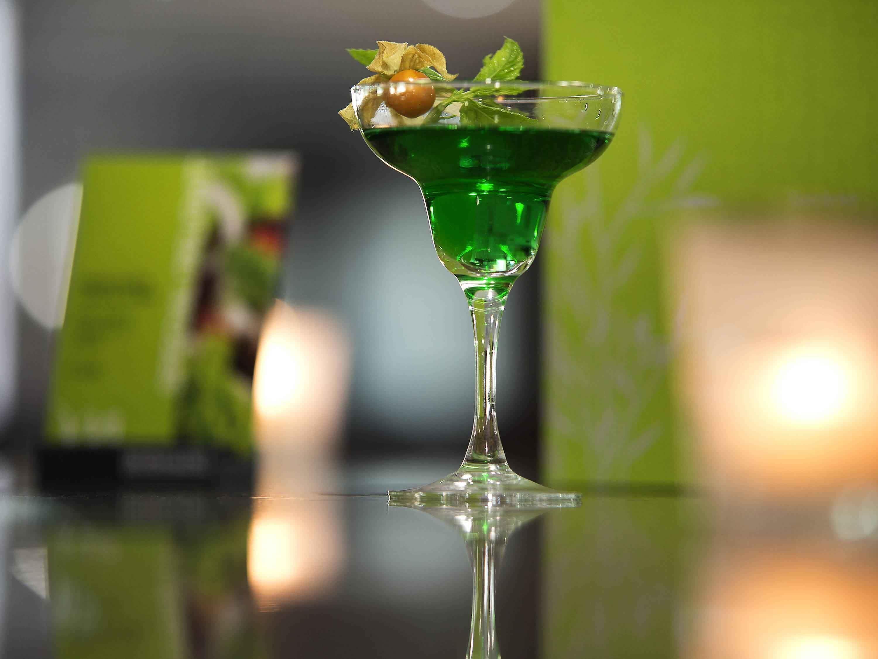 Un cóctel en una copa de martini con una guarnición sobre una superficie reflectante.
