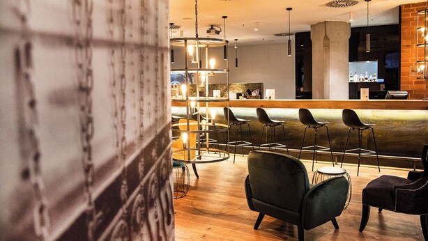 A modern bar area with a bar counter, multiple stools, and pendant lighting. - Mercure Hotel Hamm (Hamm)