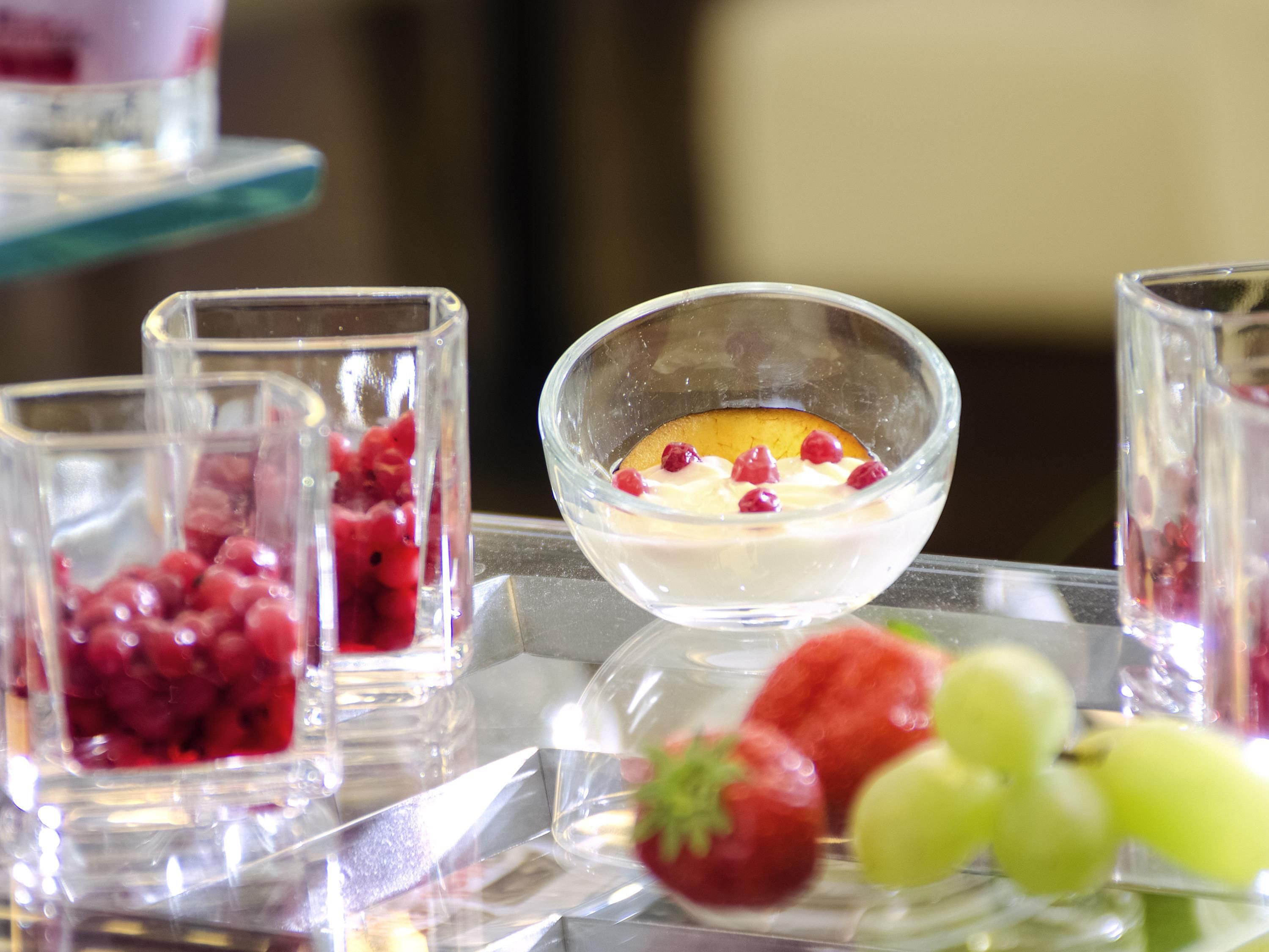 A dessert display with a bowl of yogurt topped with berries and a glass container with red berries.
