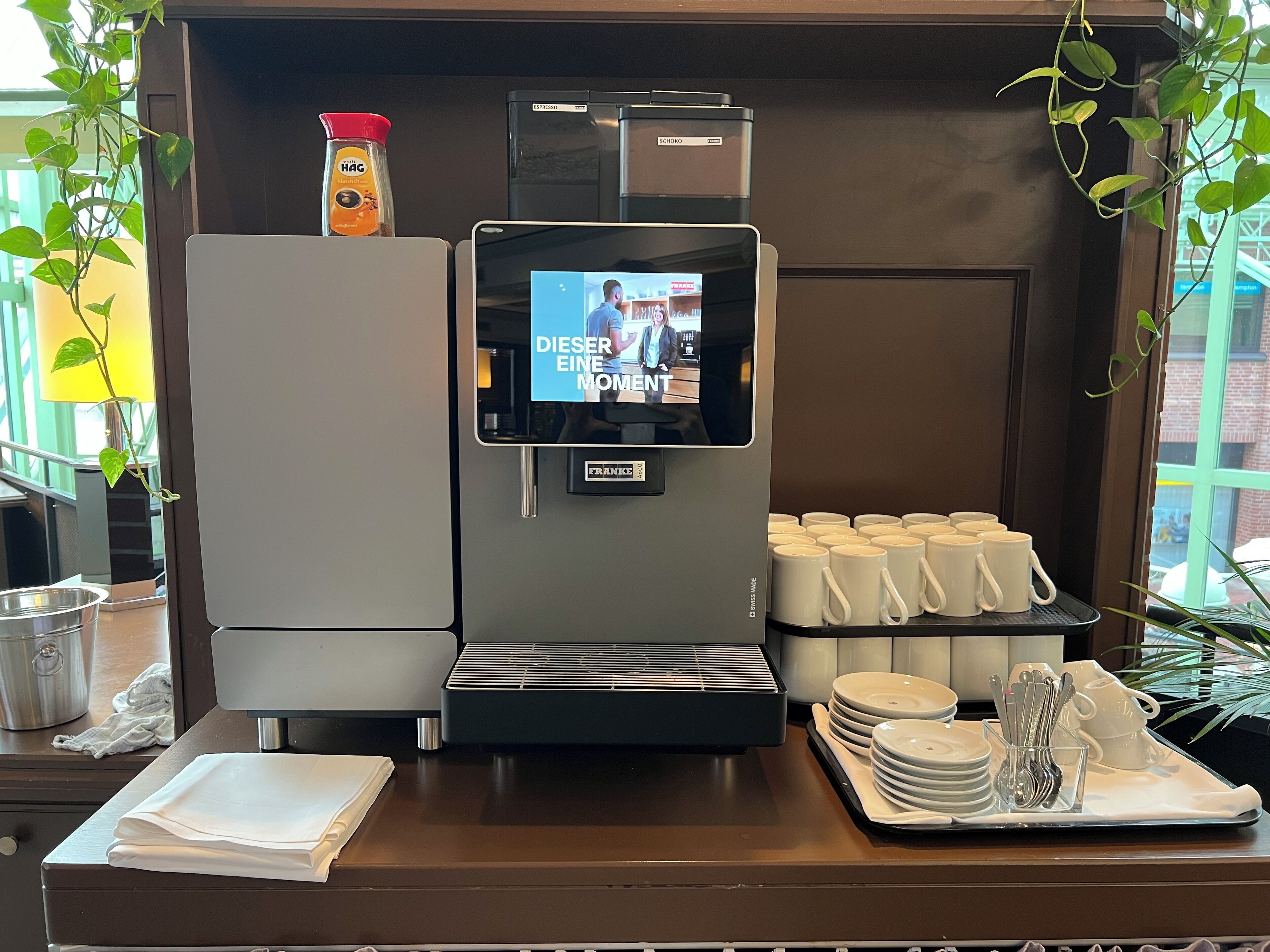 Eine Kaffeemaschine mit digitalem Display, ein Kühlschrank und ein Tablett mit Tassen und Besteck.