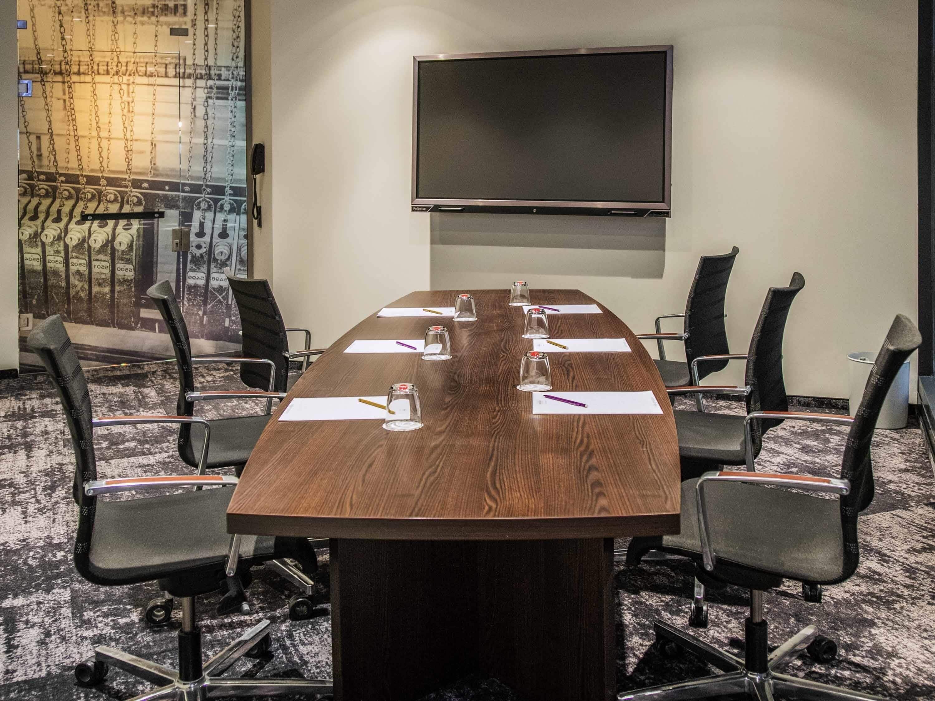 A conference room with a long table, six chairs, a flat-screen TV, and a decorative wall mural.
