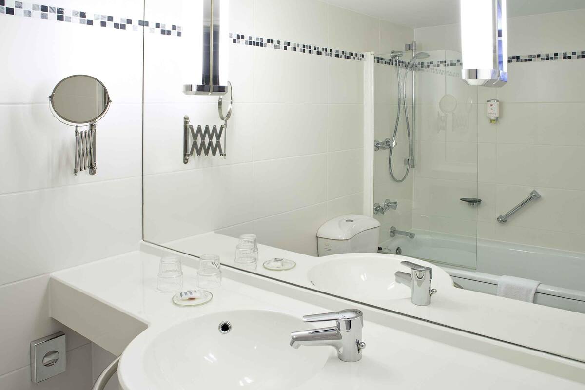 A modern bathroom with two sinks, a large mirror, a shower, and a toilet.