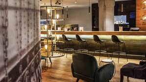 A modern bar area with wooden flooring, black bar stools, and pendant lighting. - Mercure Hotel Hamm (Hamm)