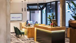 A hotel reception area with a marble reception desk, a green chair, a computer, and a sign that reads "Mercure HOTELS". - Mercure Hotel Hamm (Hamm)