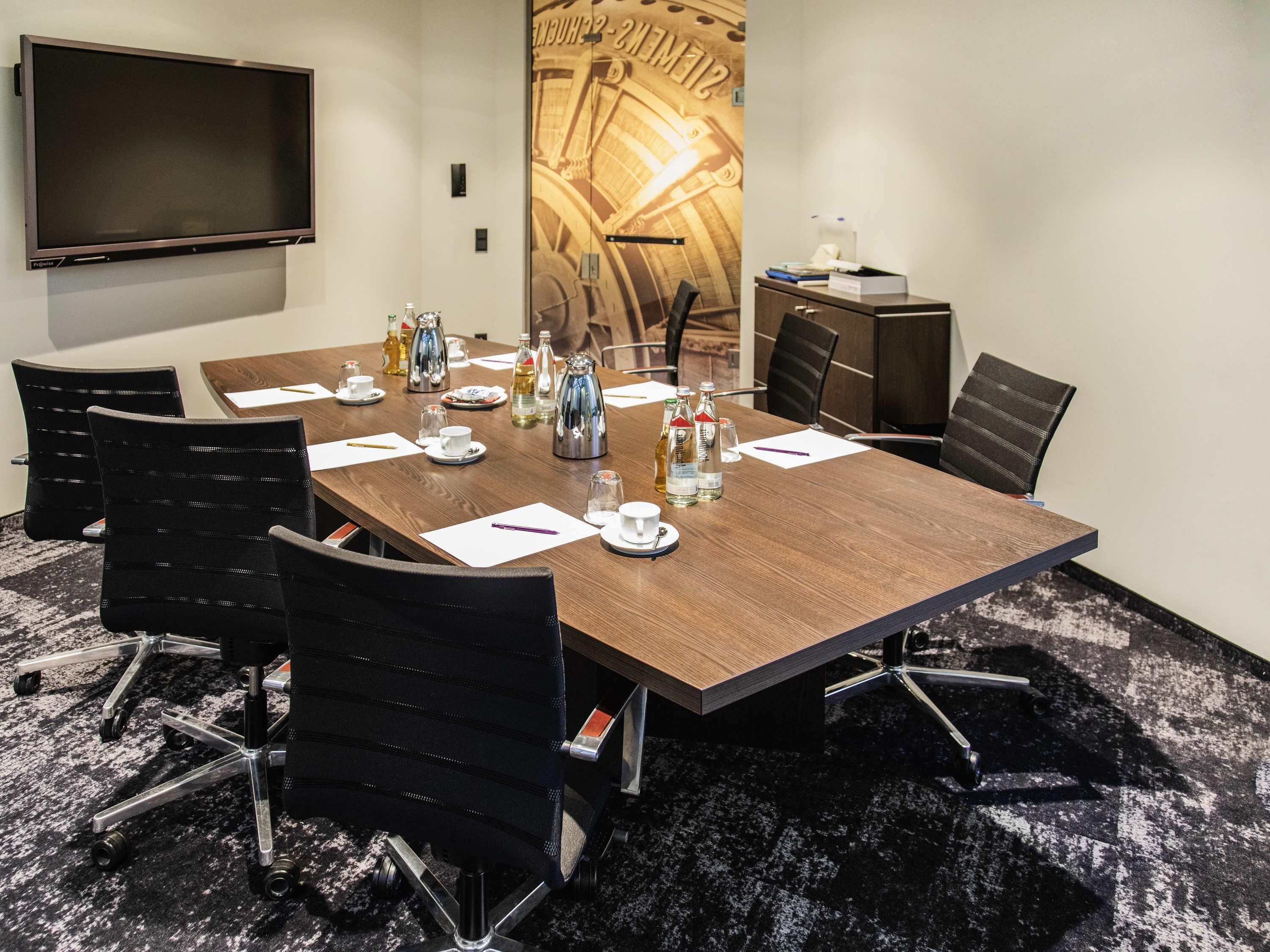 A conference room with a large table, chairs, a TV, and a decorative wall piece.