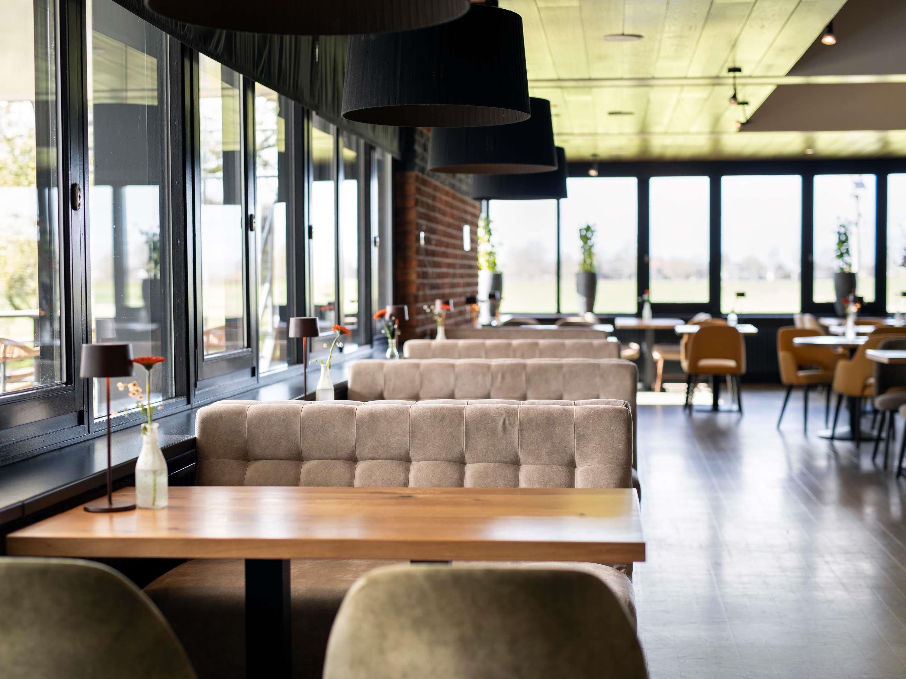 Een modern restaurant met grote ramen, zachte zitplaatsen en hanglampen.