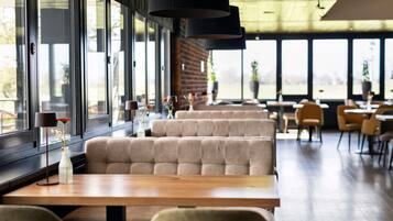 Een modern restaurant met grote ramen, zachte zitplaatsen en hanglampen.