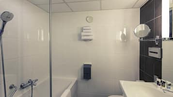 Un baño moderno con ducha de vidrio, inodoro blanco y lavamanos con espejo.