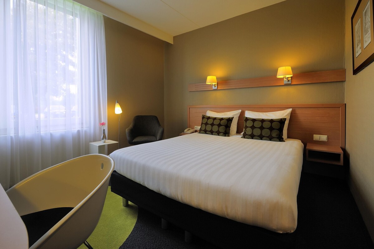 Een hotelkamer met een groot bed, twee bedlampen, een stoel en een kleine tafel met een lamp.