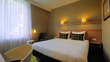 Een hotelkamer met een groot bed, twee bedlampen, een stoel en een kleine tafel met een lamp.