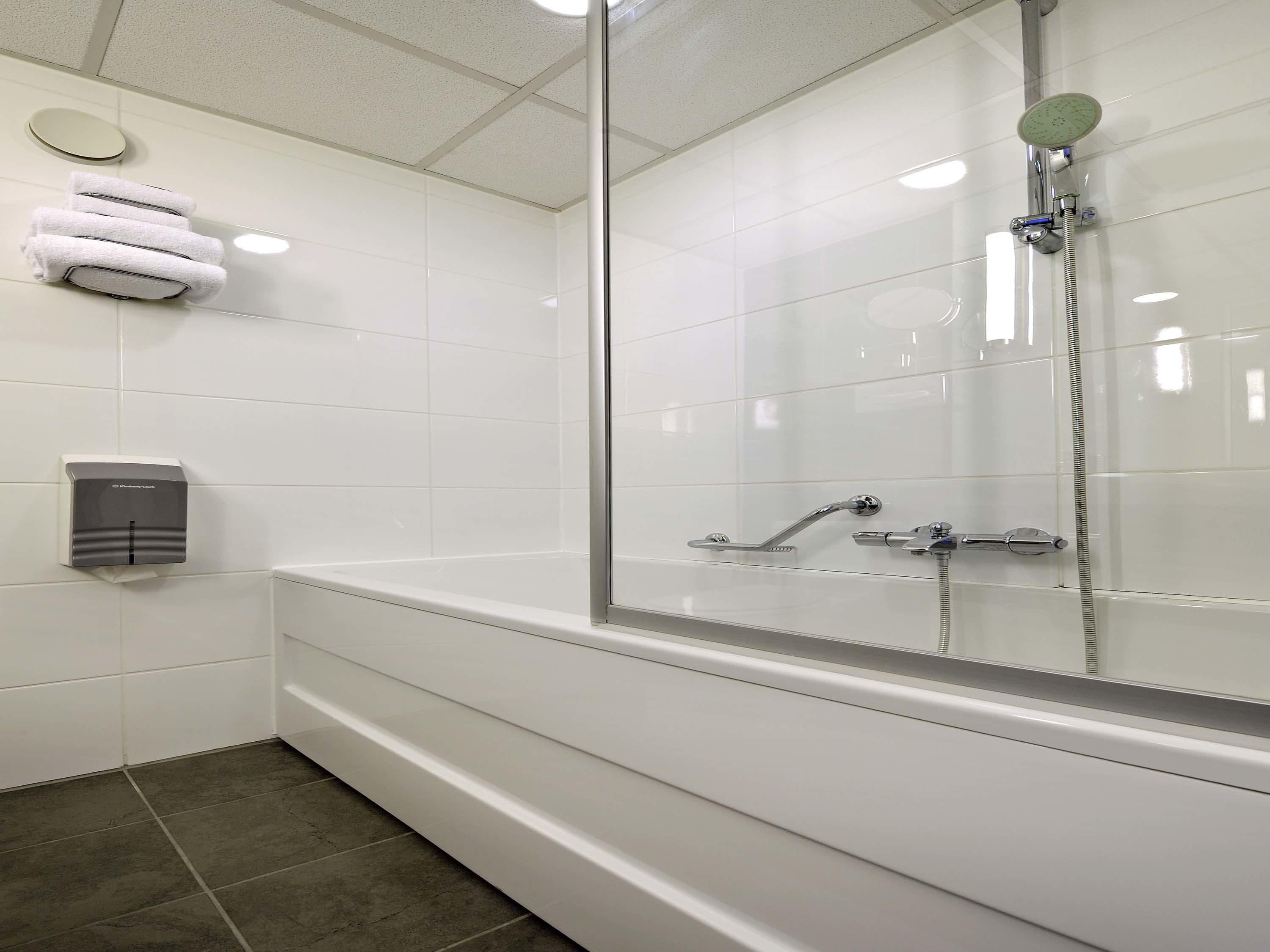 A modern bathroom with a glass-enclosed shower, a towel rack with folded towels, and a hand dryer.