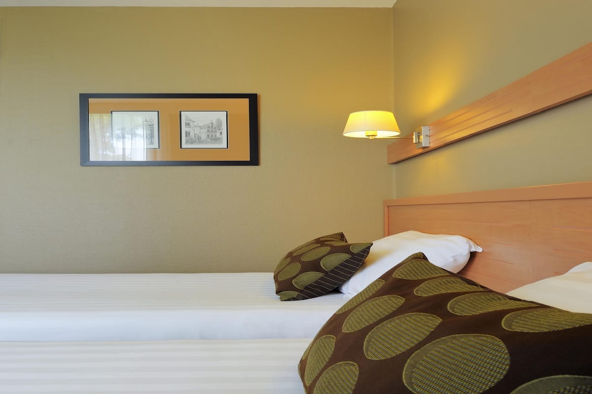 Een hotelkamer met twee bedden, een ingelijst schilderij aan de muur en een wandlamp.