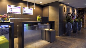 A modern reception area with a reception desk, two monitors, and decorative vases. - Mercure City Zwolle Hotel (Zwolle)