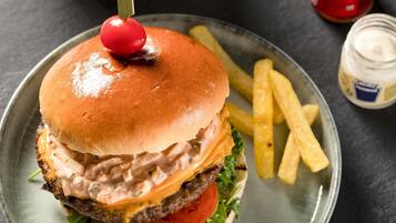 Una hamburguesa con cereza encima, acompañada de papas fritas y un frasco de kétchup.