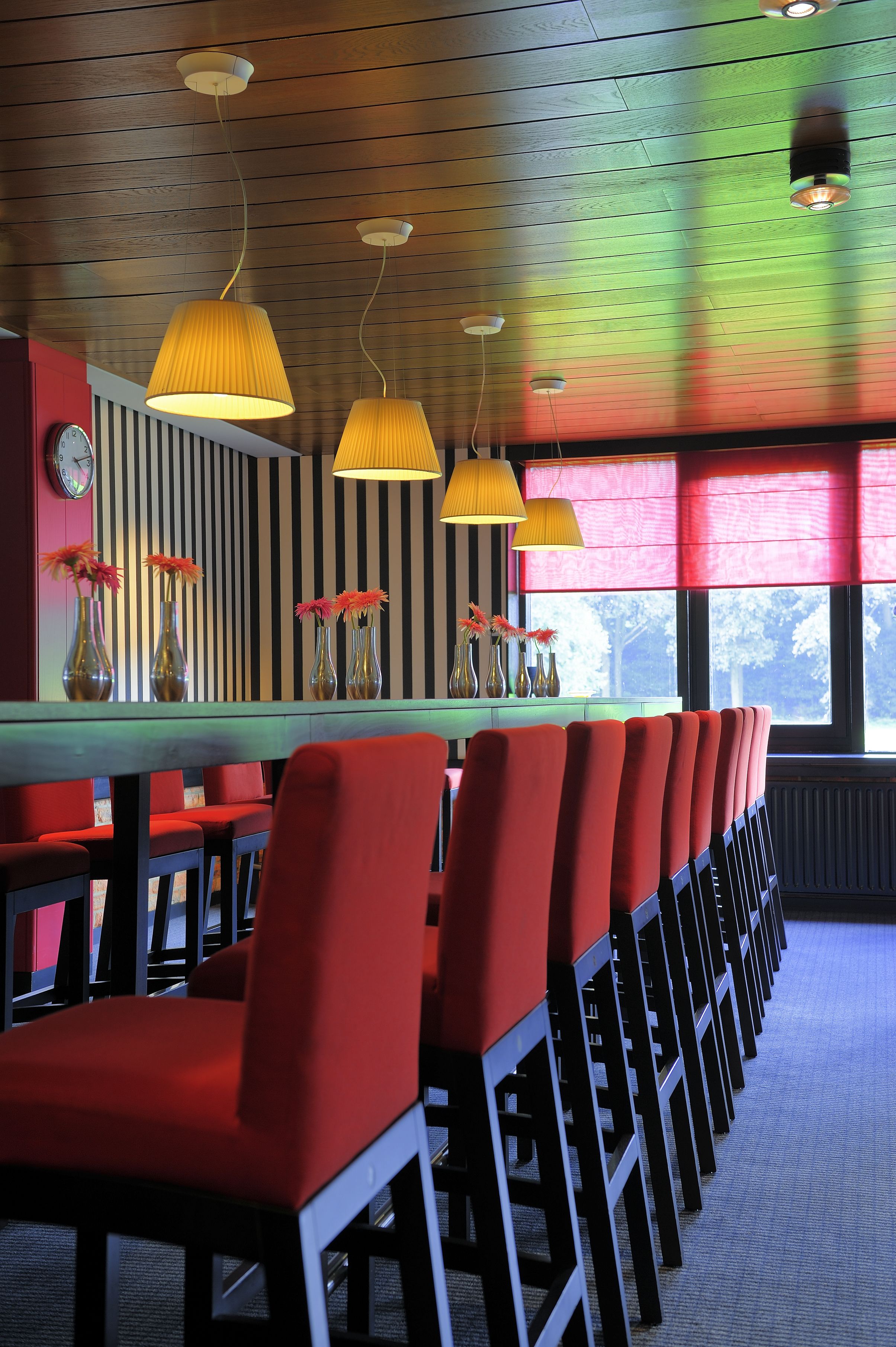 Une salle de conférence avec une longue table, des chaises rouges et des lampes suspendues.