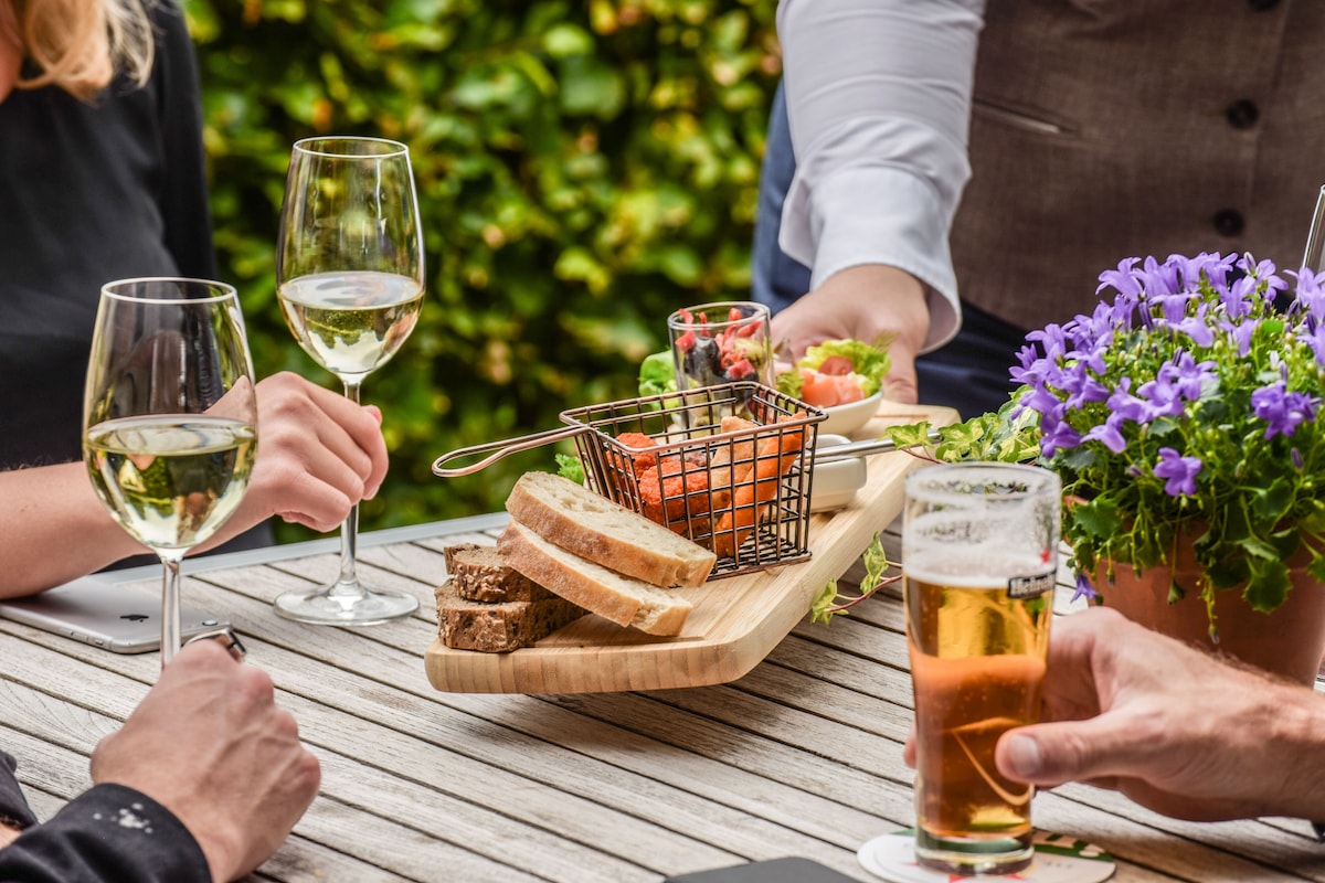 Een houten tafel met een mand vol brood, een glas bier en een glas witte wijn.