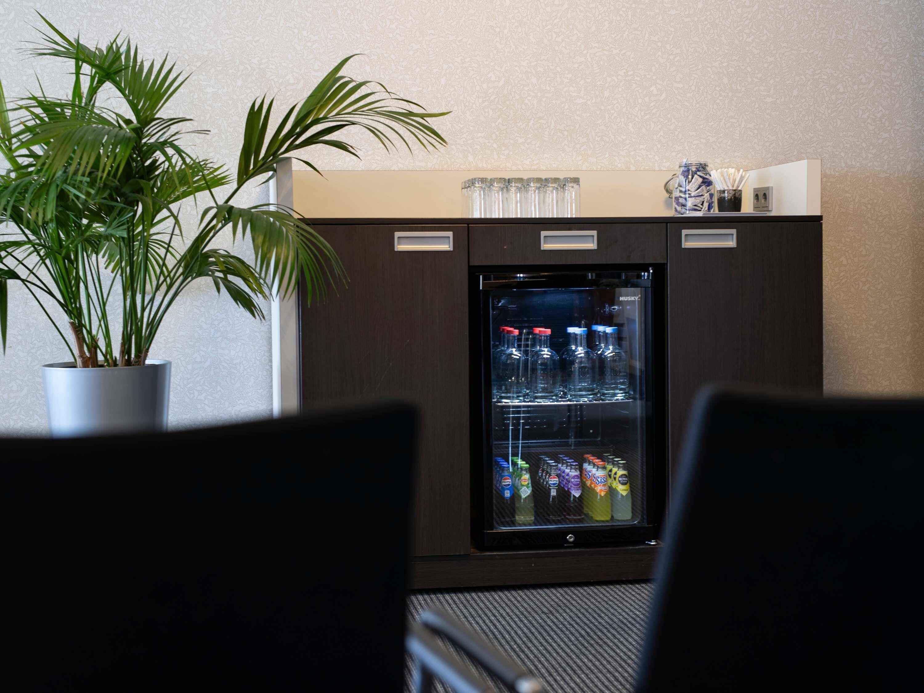 A minibar with a beverage dispenser, a potted plant, and a small decorative item on top.