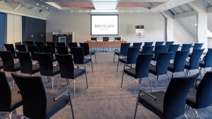 Een vergaderzaal met rijen stoelen, een presentatiescherm en een spreekgestoelte.