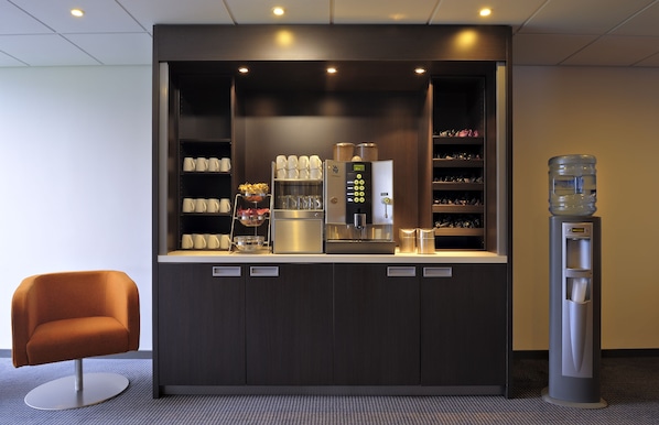 Een moderne kitchenette met een koffieapparaat, waterkraan en opbergplanken.