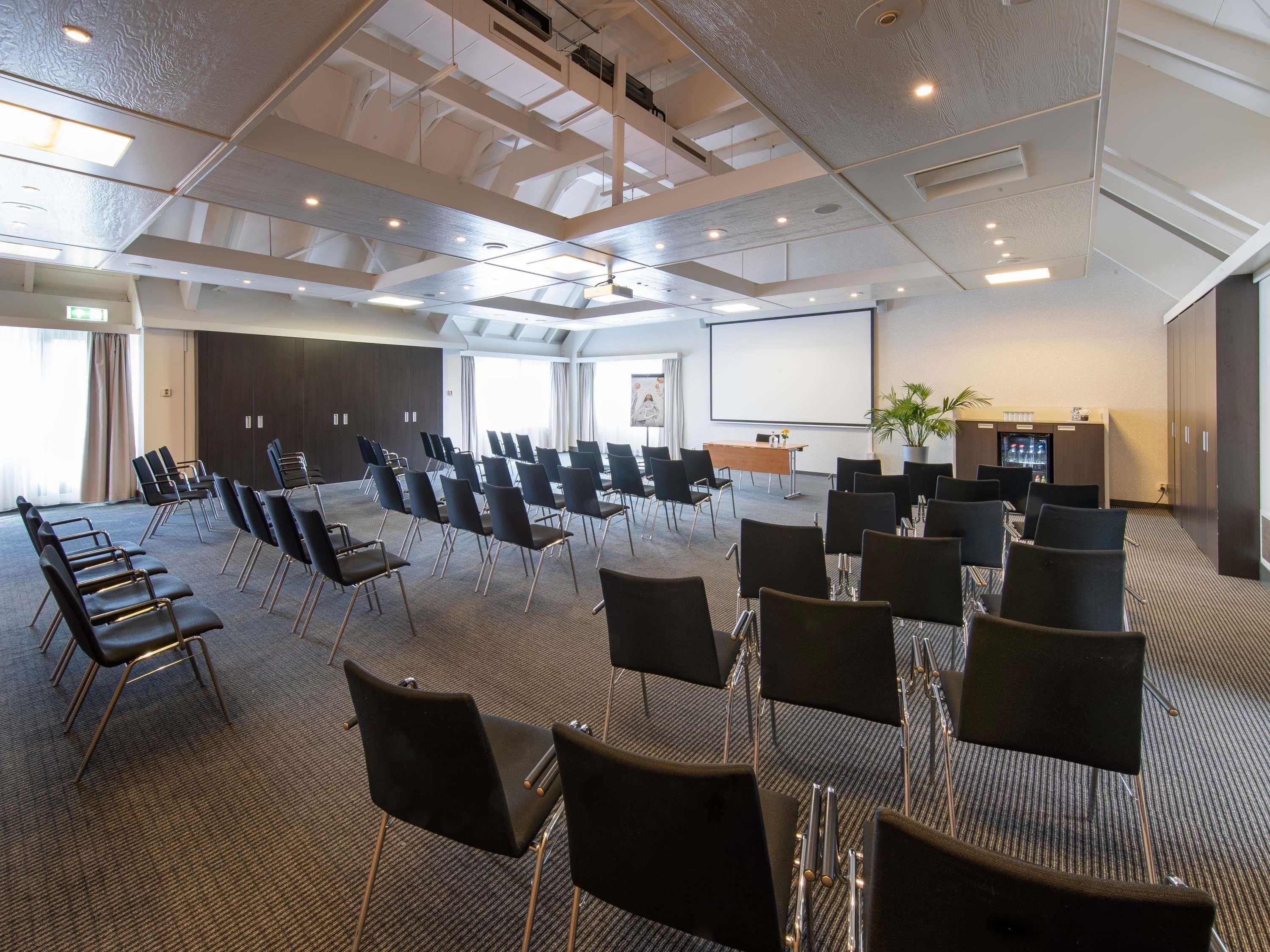 A conference room with rows of chairs, a projector screen, and a presentation area.