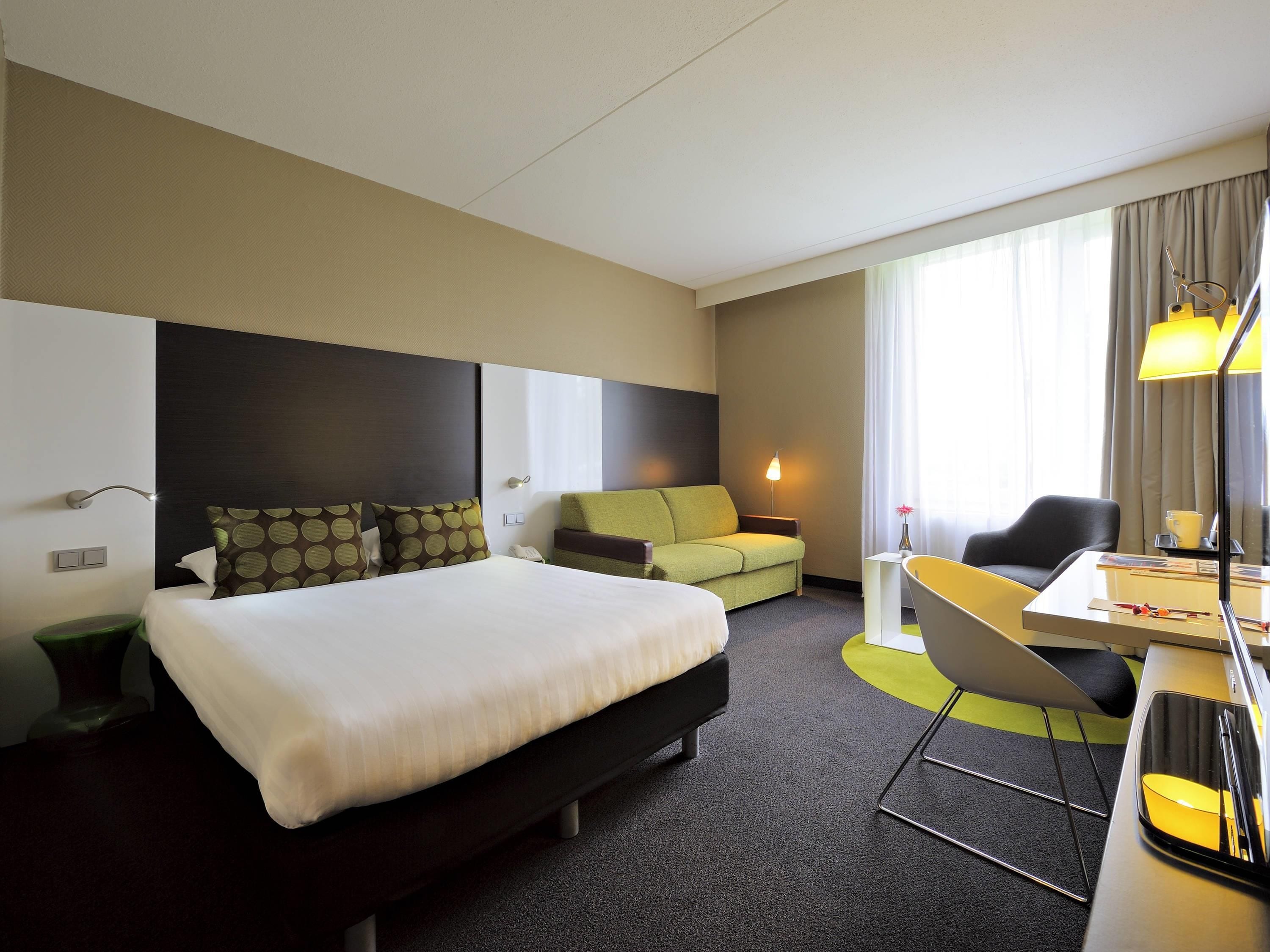 A hotel room with a bed, a sofa, a desk, and a chair.