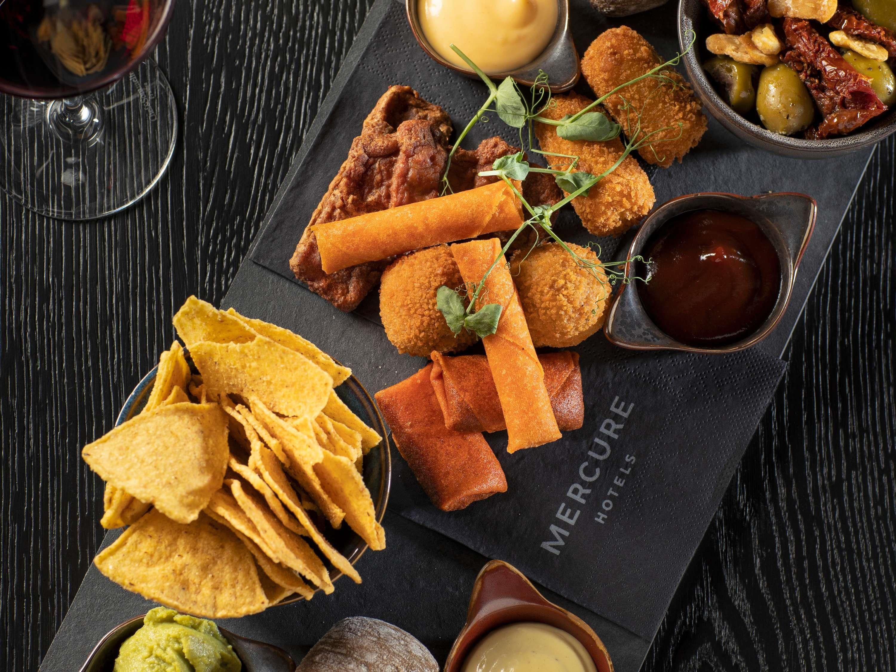 A variety of appetizers including fried items, chips, and dips, arranged on a slate board.