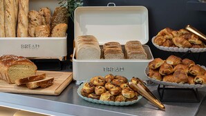 A buffet with various breads and pastries, including baguettes, croissants, and a plate of muffins. - ibis Styles Angouleme Nord (Champniers)