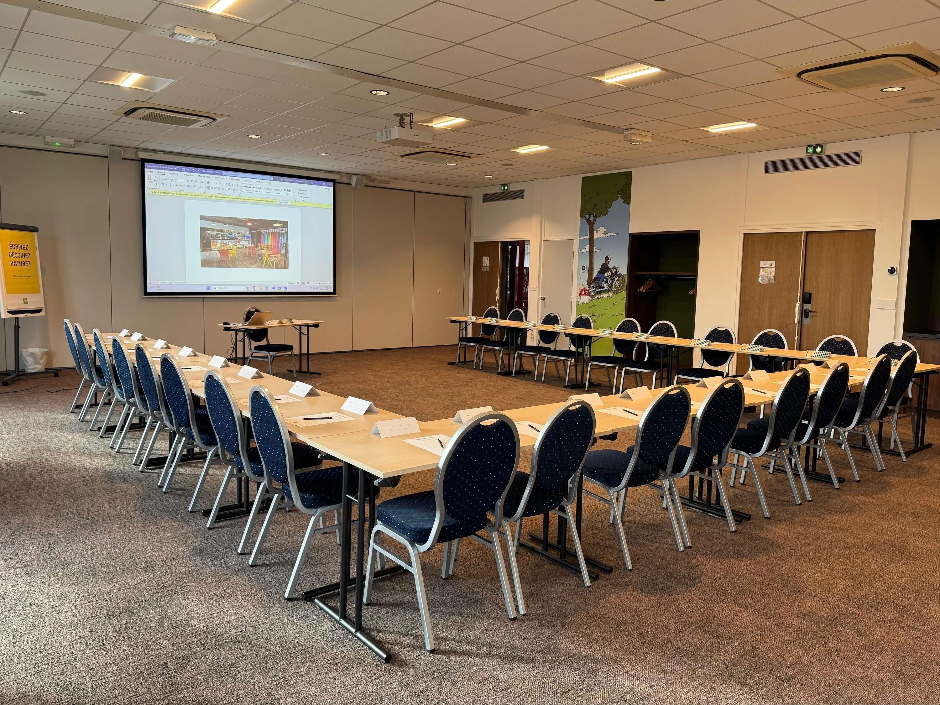 A conference room with a large screen, multiple tables, and chairs.