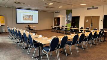 A conference room with a large screen, multiple tables, and chairs.