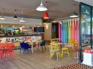 A brightly colored bar area with tables and chairs, a television, and a colorful wall mural.