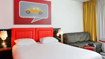Una habitación de hotel con una cama, un cabecero rojo, un sillón gris, una ilustración de un coche amarillo en la pared y una ventana con cortinas amarillas.