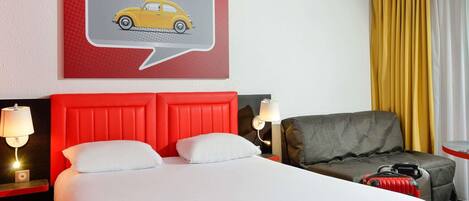 A hotel room with a bed, a red headboard, a gray armchair, a yellow car illustration on the wall, and a window with yellow curtains.